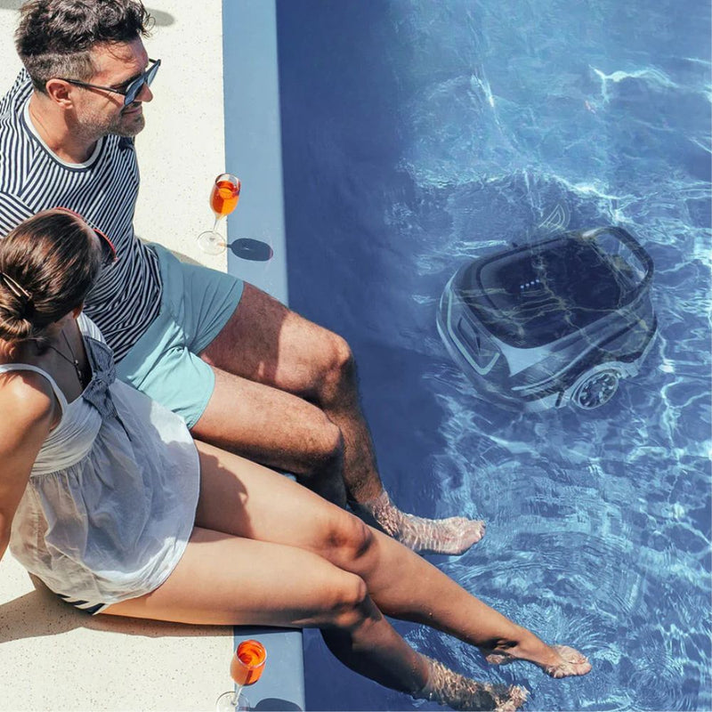 Paar sitzt entspannt am Poolrand mit Getränken, während ein Poolreinigungsroboter im Wasser automatisch reinigt.